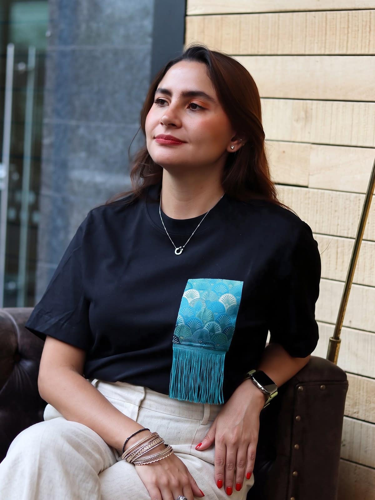 Bolsillo en brocado de conchas turquesa con flecos sobre camiseta negra de algodon
