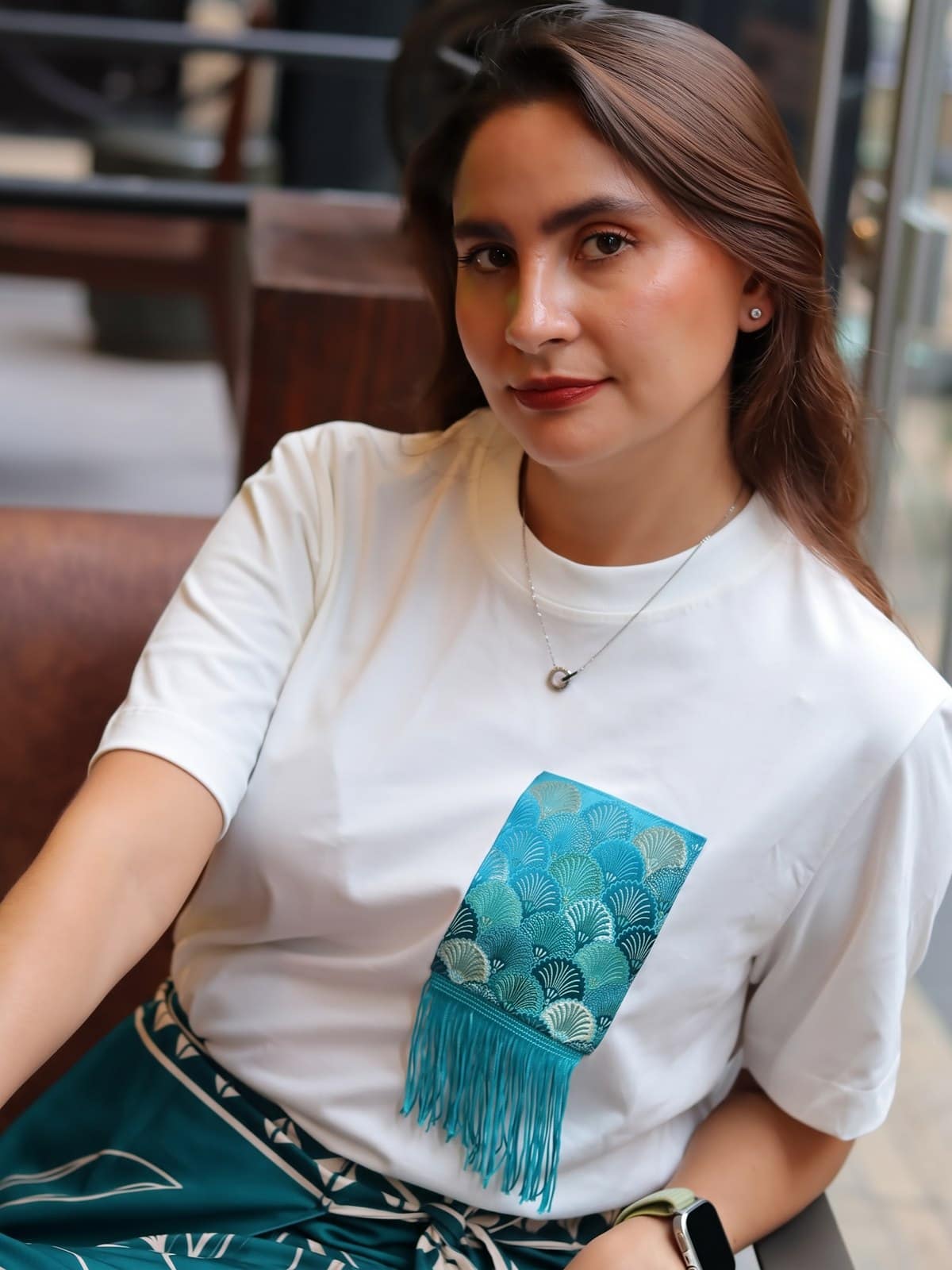 Detalle del bolsillo en brocado de conchas turquesa sobre camiseta blanco hueso