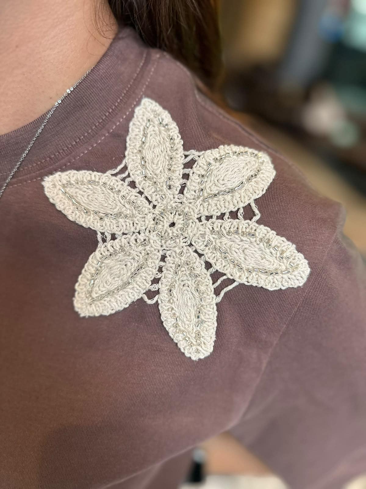 Detalle de la flor tejida color hueso sobre la camiseta café